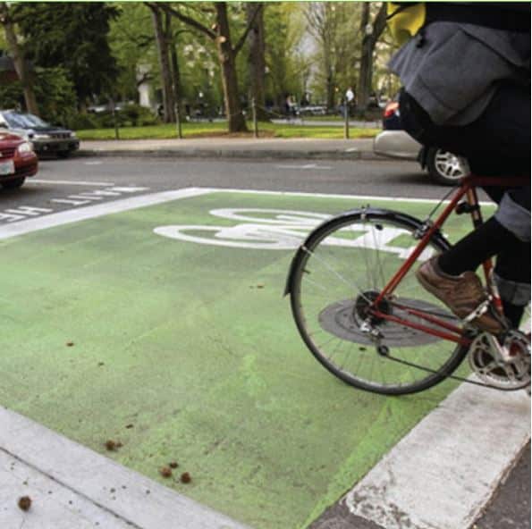 Green box painted on pavement with bicycle riding on it in traffic