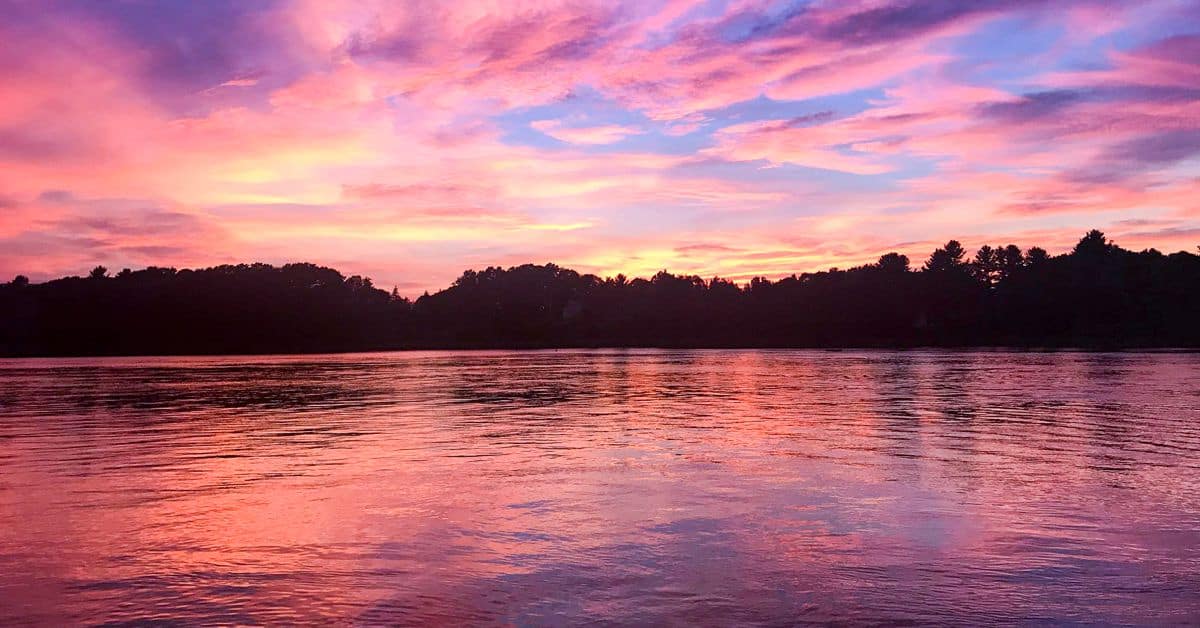 Pink and purple sunset image over water with tree skyline of Great Bay Estuary